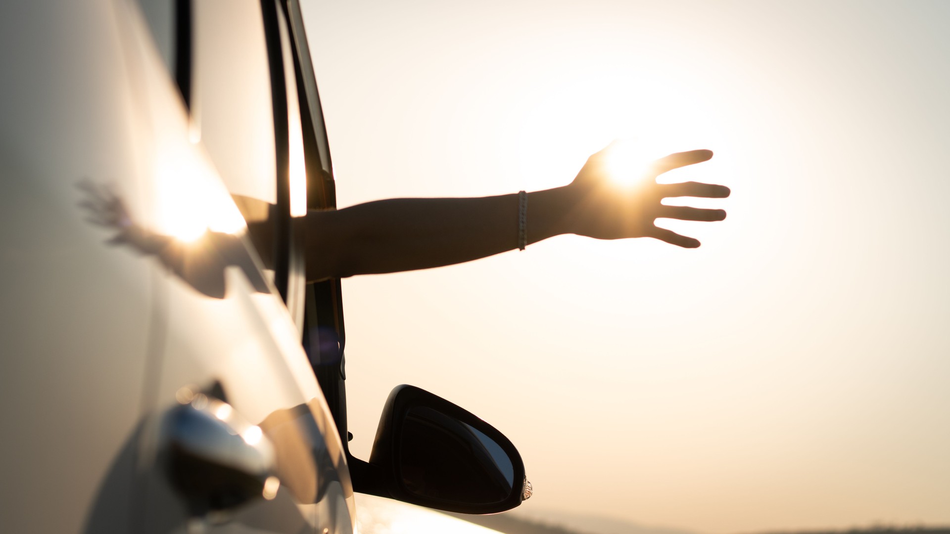 Hatchback Car travel driving road trip of man summer vacation in white car at sunset, happiness to travel, enjoy vacation and relax, male driver extends his hand out the car window while driving